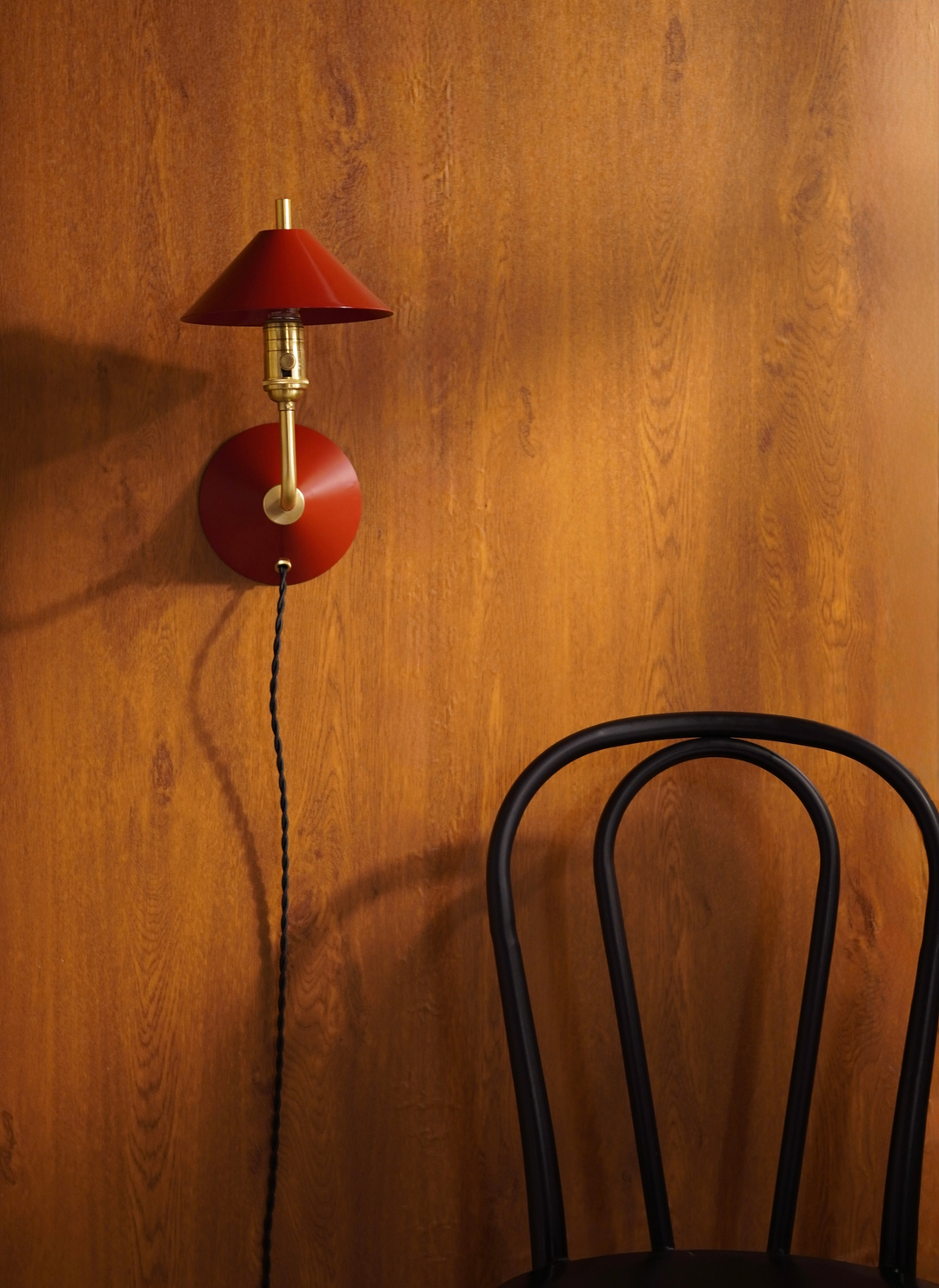 Red wall lamp with a black chair against a wooden wall